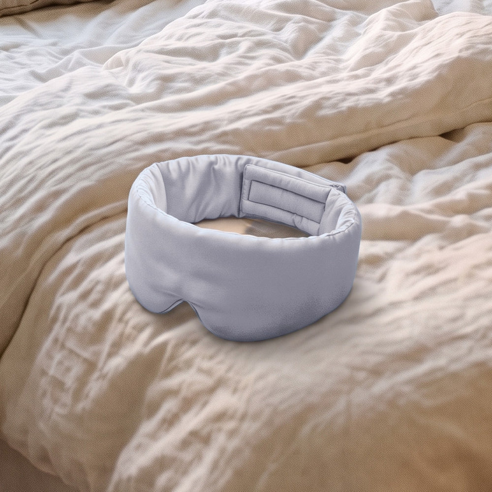 The Vespré Silk Sleep Mask in Silver resting on a linen bed in morning light