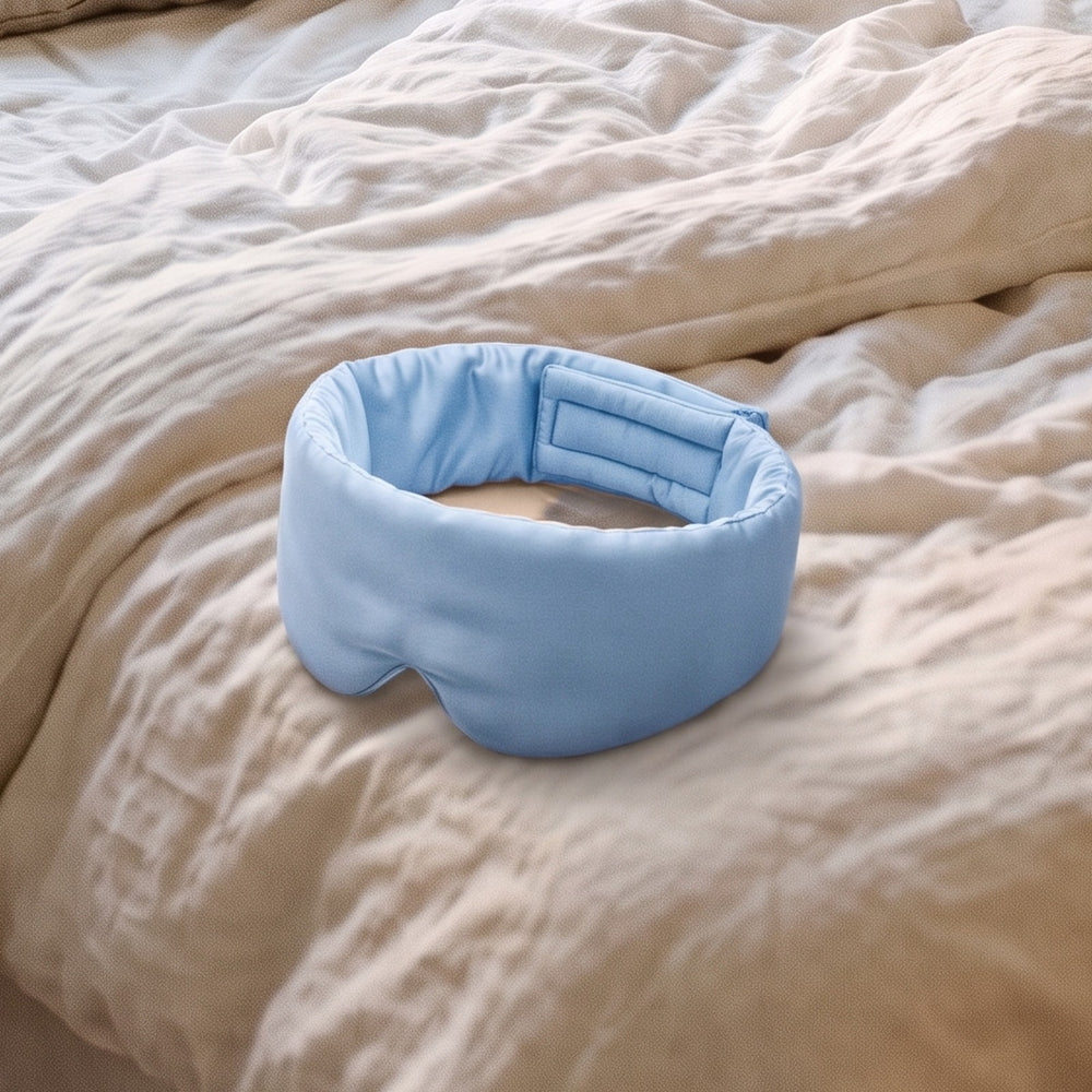 The Vespré Silk Sleep Mask in Sky Blue resting on a linen bed in morning light