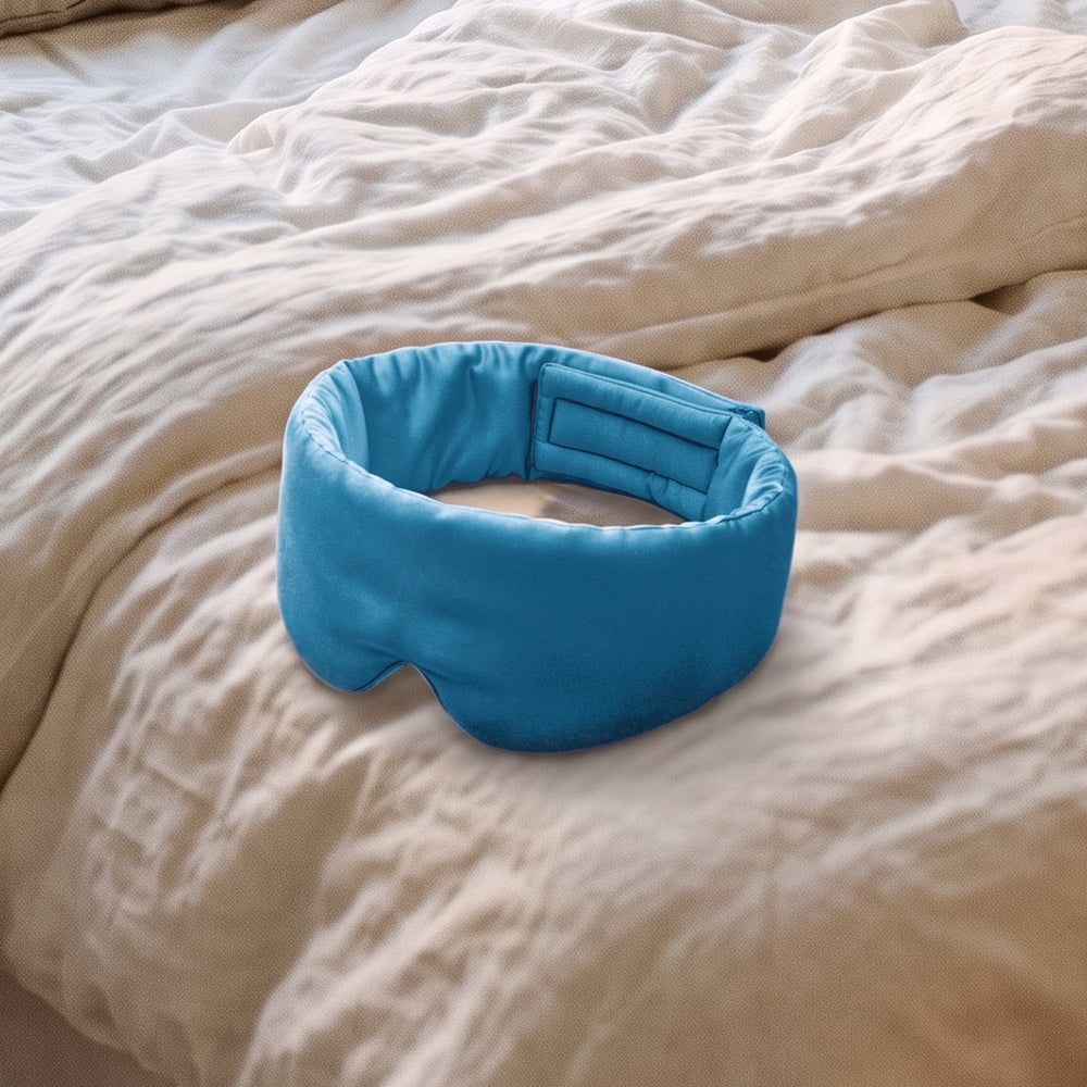 The Vespré Silk Sleep Mask in Teal resting on a linen bed in morning light
